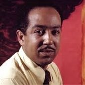 Photo of Langston Hughes posing in front of a red background.