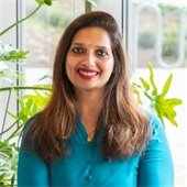 Image of Director of Libraries Sonal Rastogi, wearing a blue blouse and sitting in front of a plant.