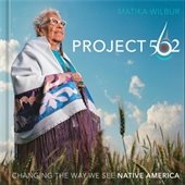Elderly person wearing a colorful traditional shawl stands proudly in a wheat field under a blue sky. The Book title is "Project 562: Changing the Way We See Native America."