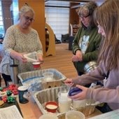 Women engage in a craft activity at a table with colorful materials and containers. The atmosphere is lively and collaborative.