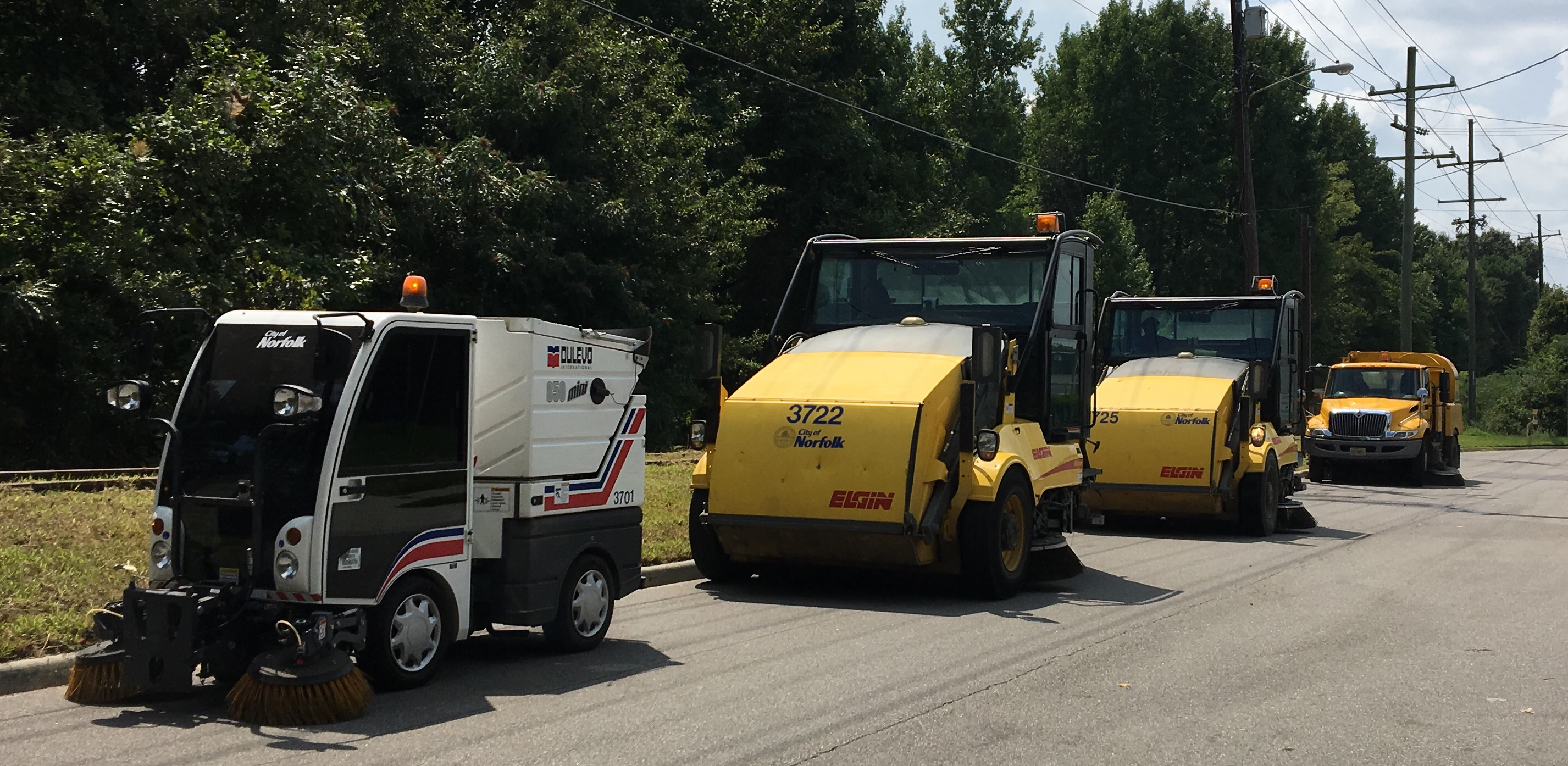 4 street sweepers, one Tymco, two Pelicans, one Global, in a row along a curbline, 